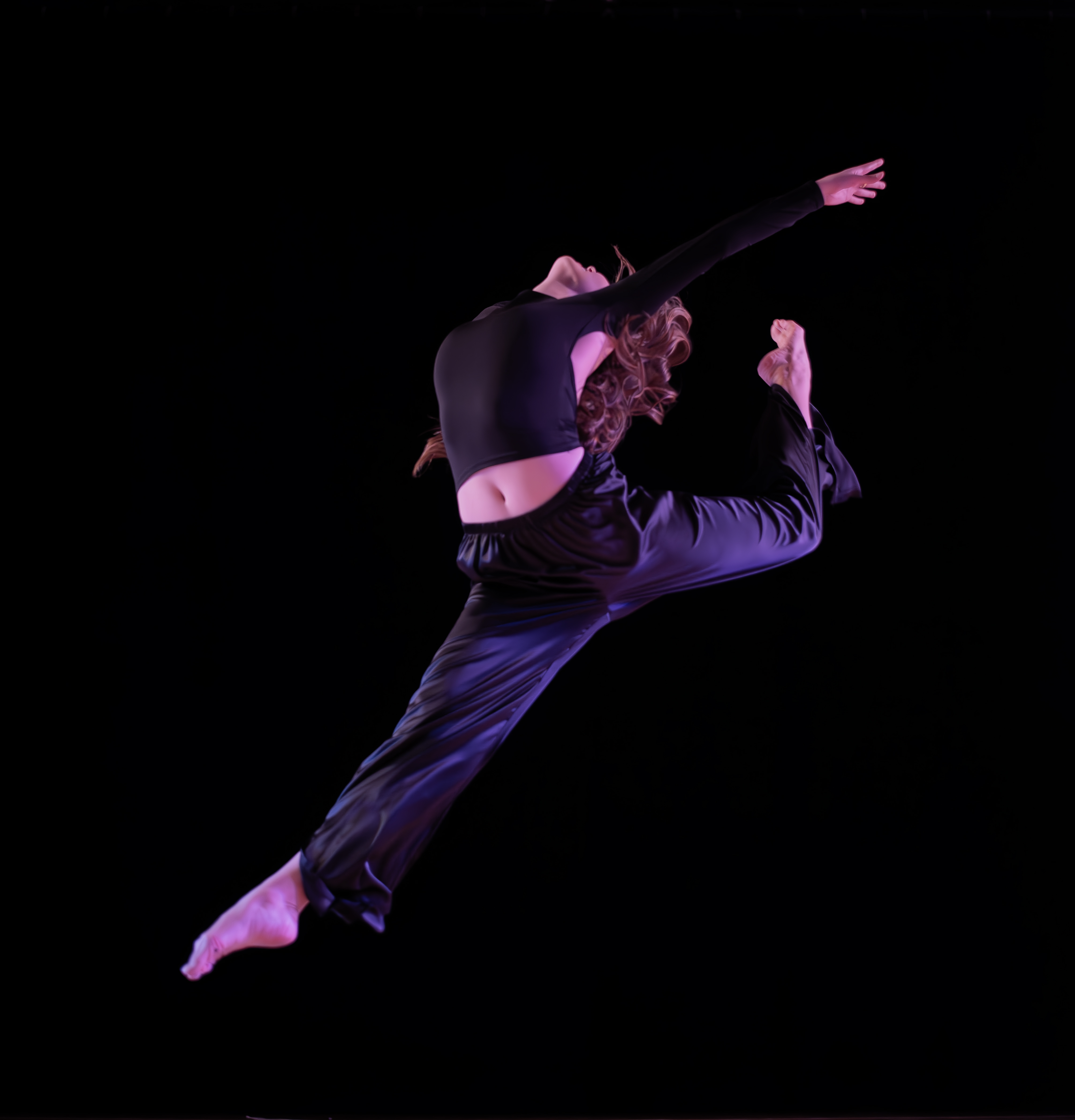 A dancer leaps exuberantly against a black background